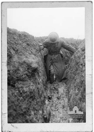 Image of Captain C E W Bean, Official War Correspondent, knee deep in mud in Gird trench, near Gueudecourt in France, during the winter of 1916-1917.